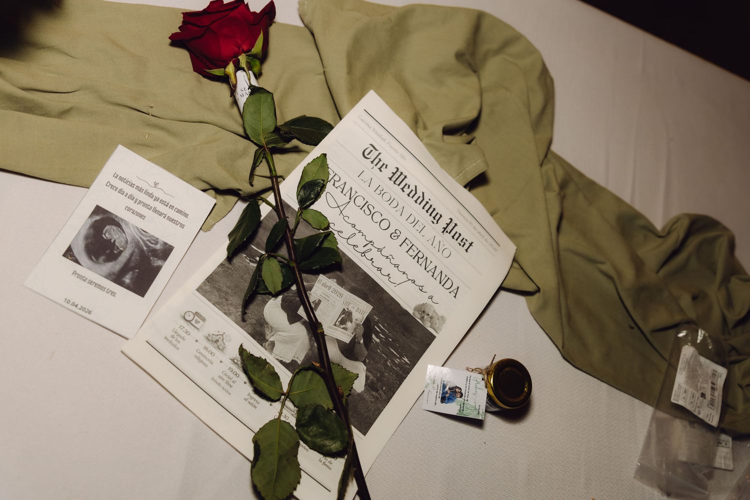 A red rose rests on a wedding newspaper keepsake and sage green jacket.