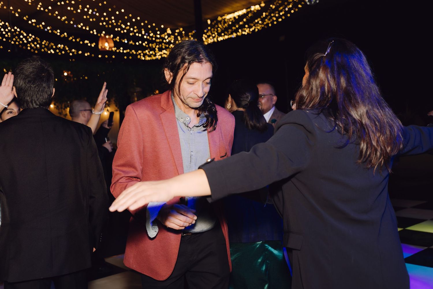 Guests dance energetically under string lights at a lively wedding reception.