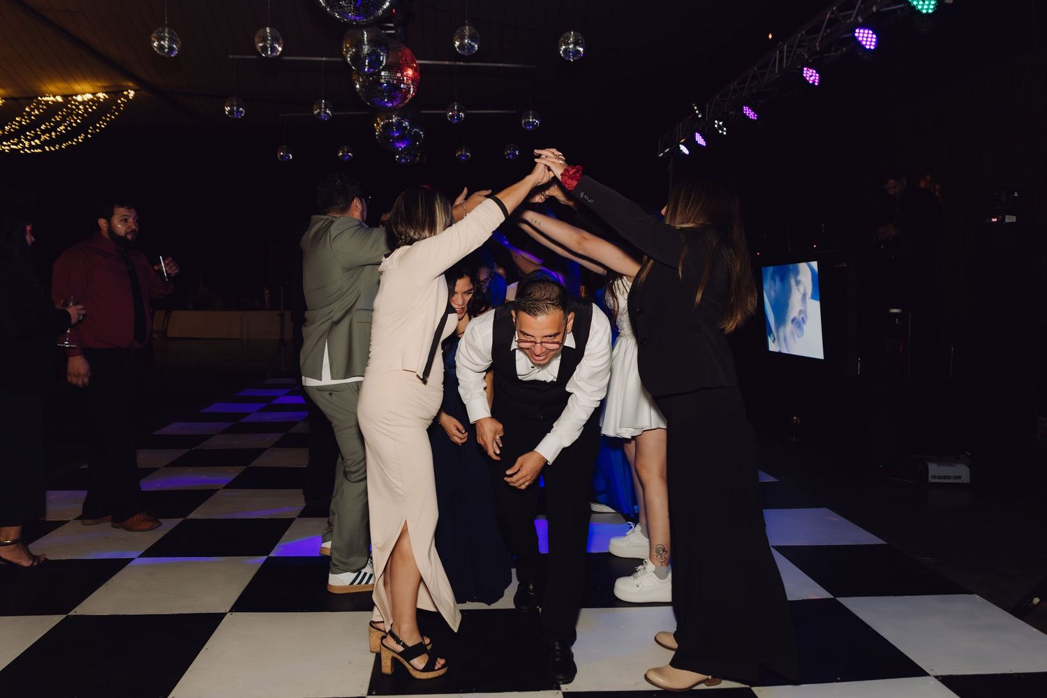 Guests dancing under disco balls on a black and white checkered dance floor at a formal party.