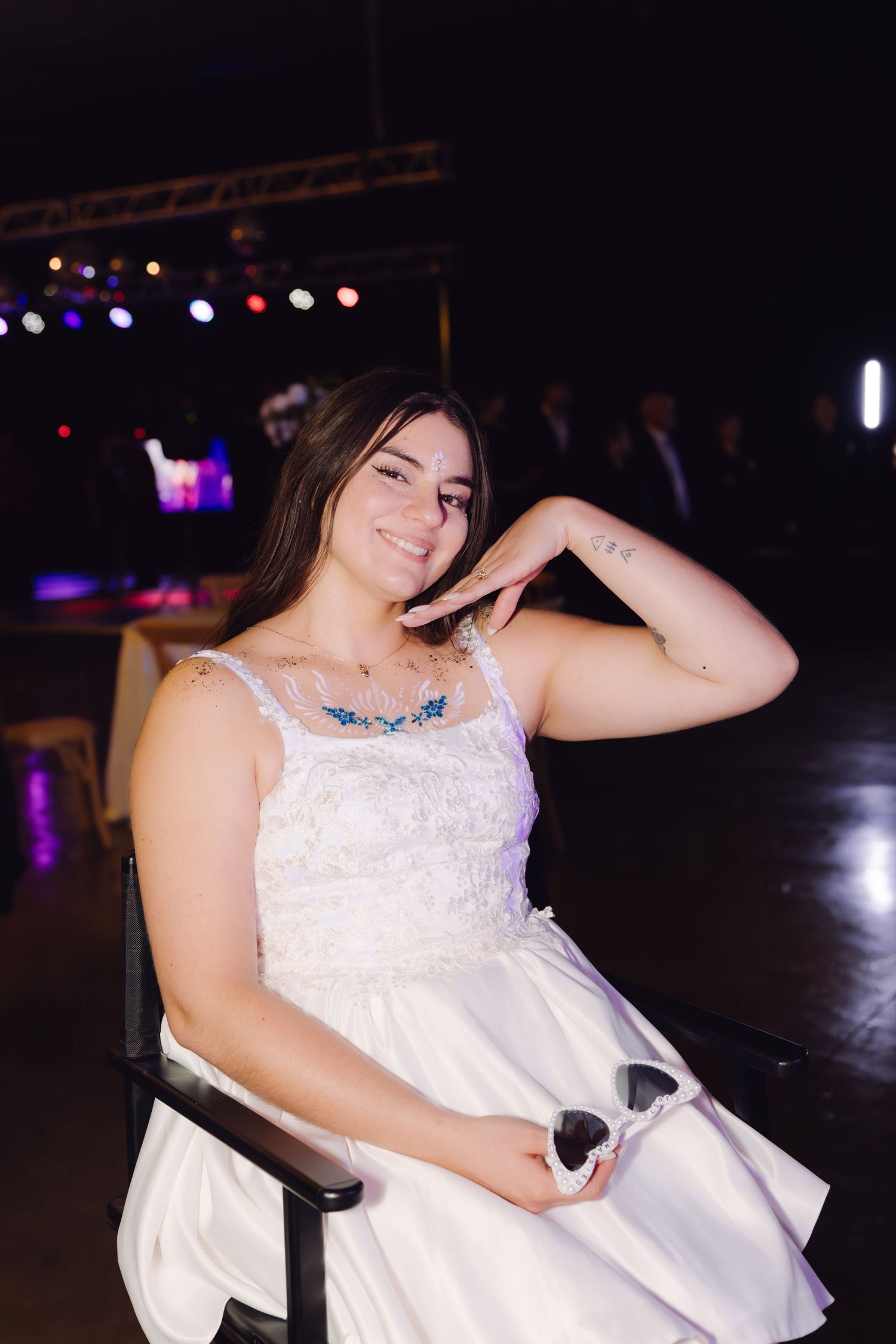Young woman in a white formal dress sitting and smiling at an elegant evening party event.