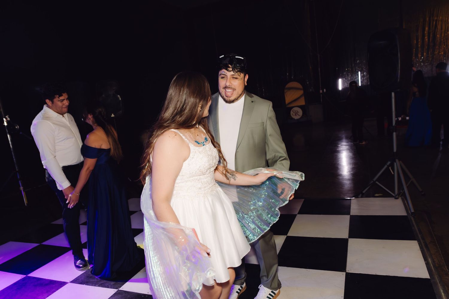 Young couple dancing together on a black and white checkered floor at a formal evening celebration.