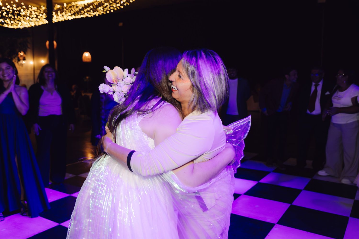 Bride and older woman sharing emotional hug on checkered dance floor at wedding reception.