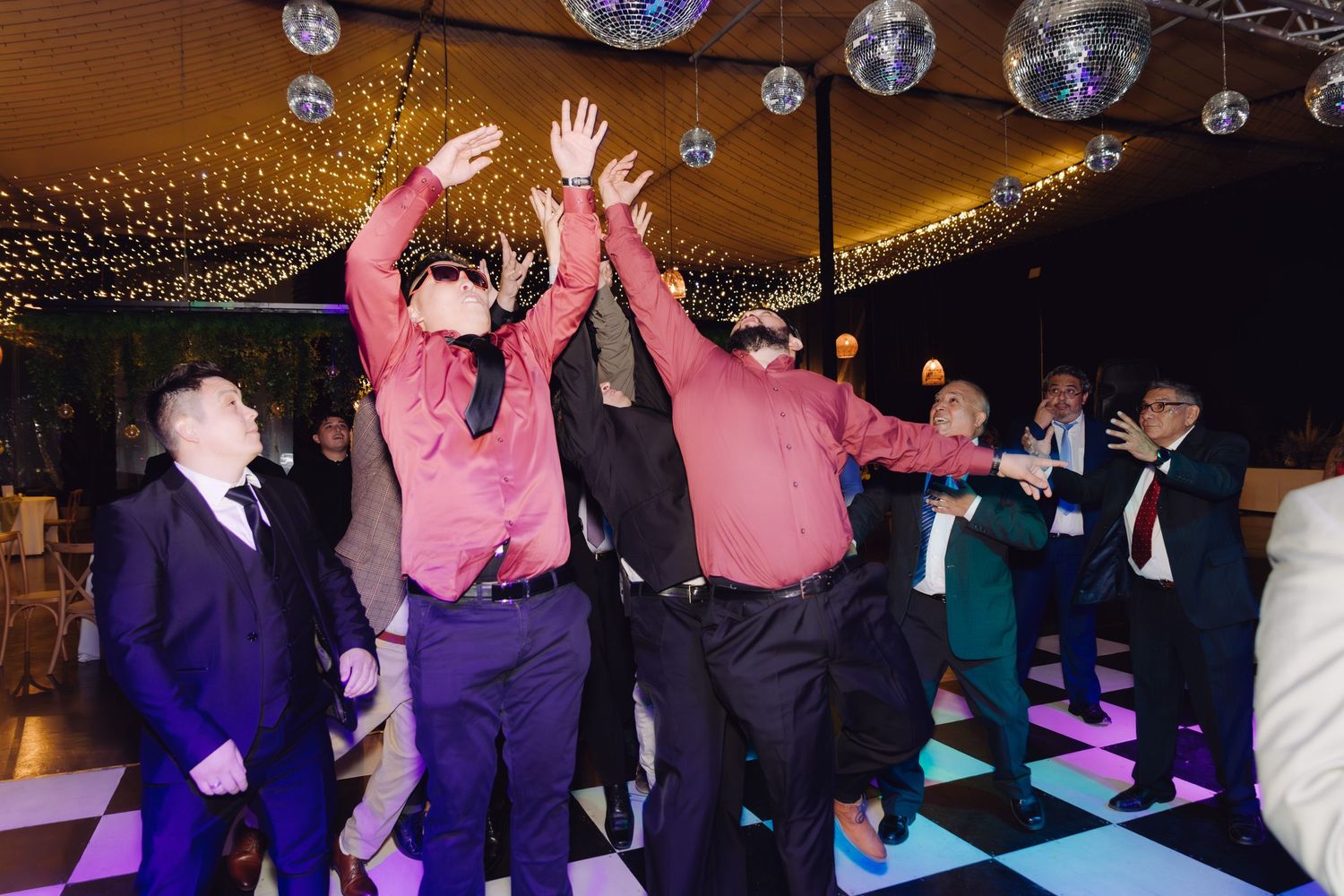 Group of men dancing energetically on checkered dance floor at wedding reception party.