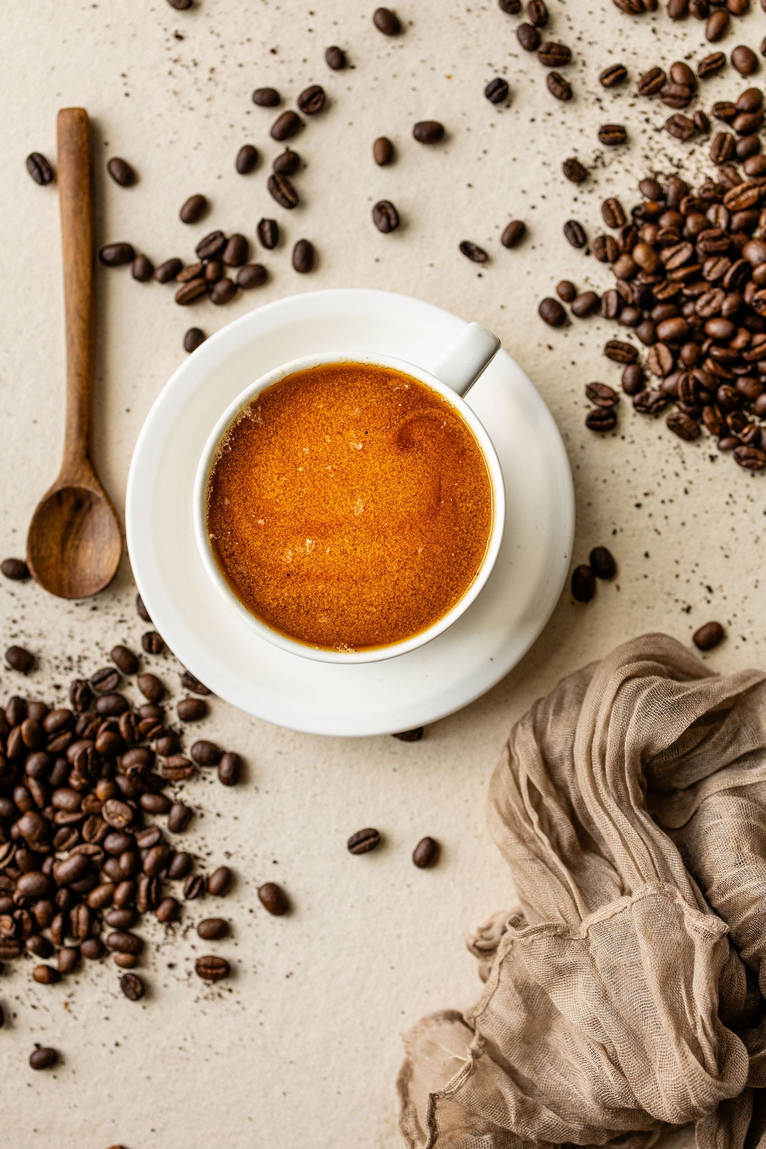 A vibrant cup of coffee against a burlap table setting with scattered beans and a linen table runner.