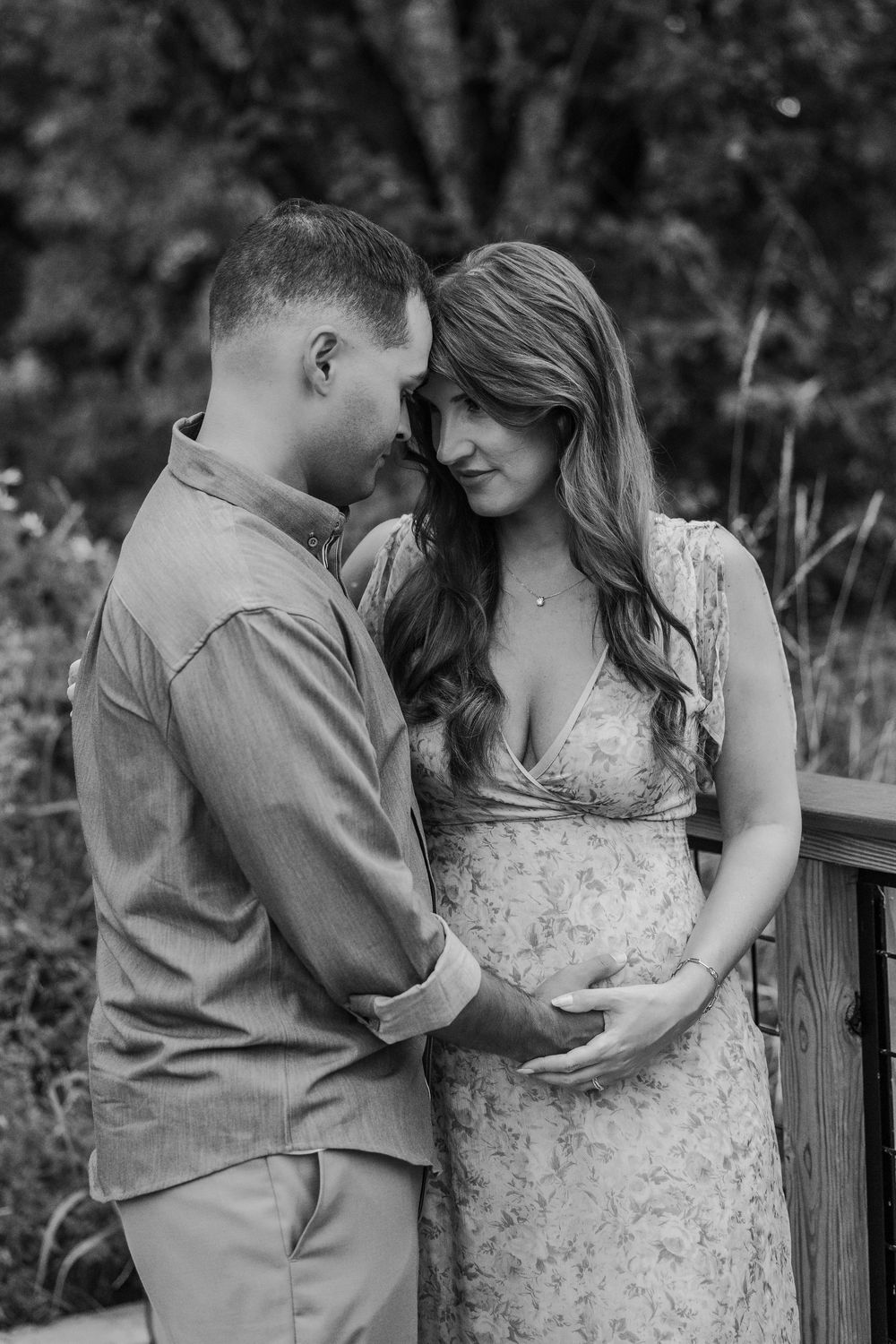 Black and white photo of a couple tenderly sharing a moment, with the woman cradling her pregnant belly outdoors.