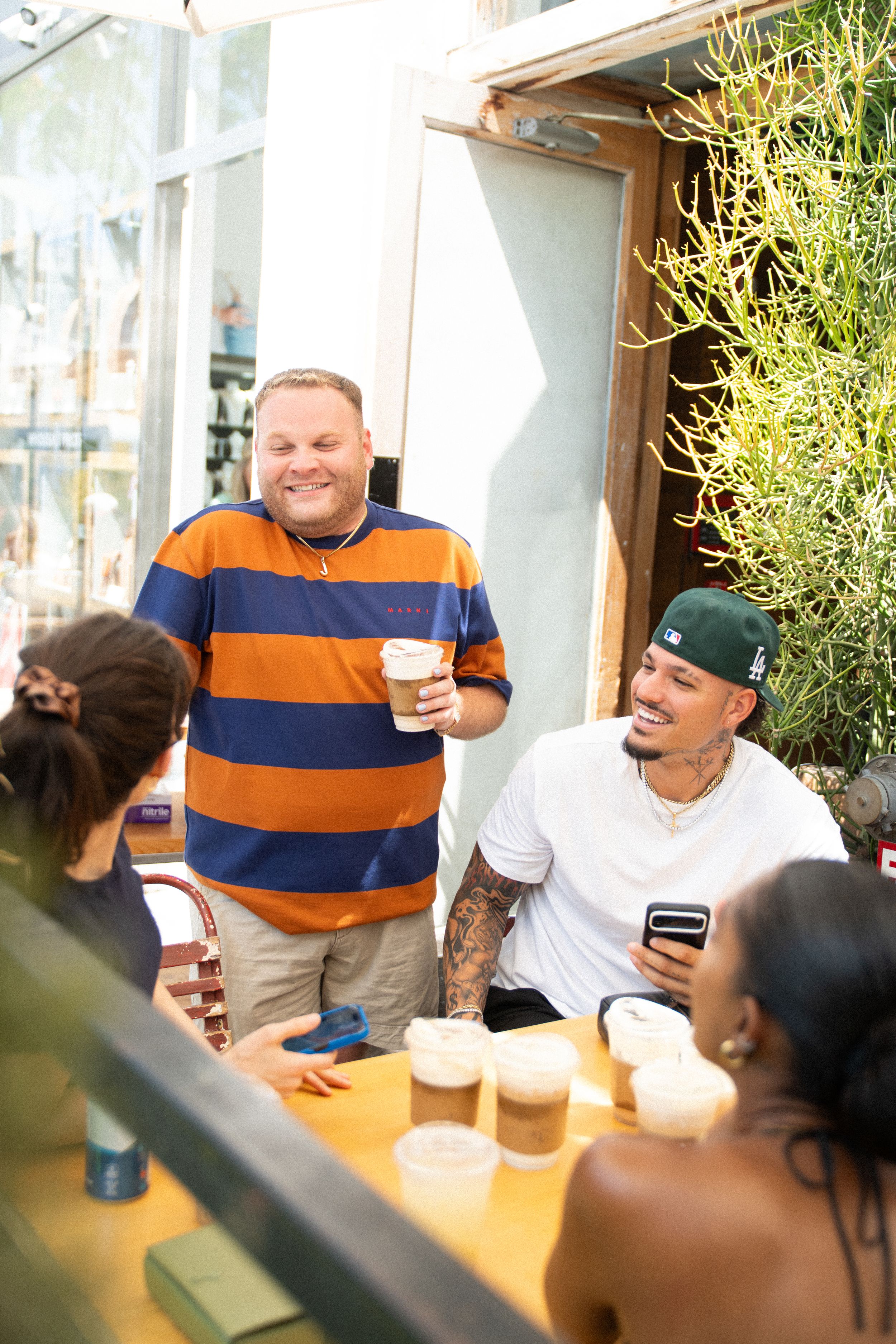 Friends socializing at an outdoor cafe, enjoying iced coffee drinks and laughing together on a sunny day.