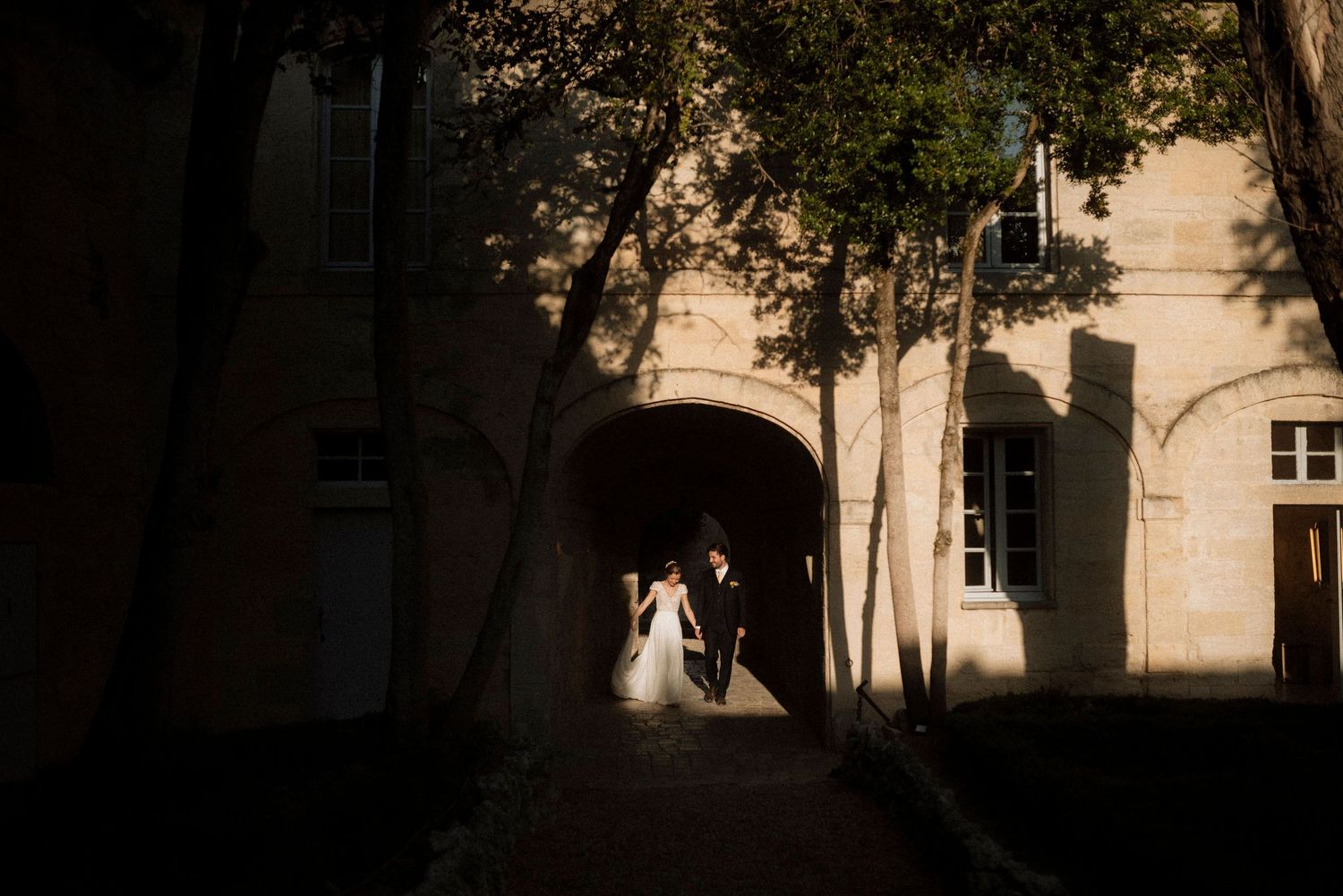 A joyful couple laughs while walking through a grassy field with a wedding tent in the background at sunset.