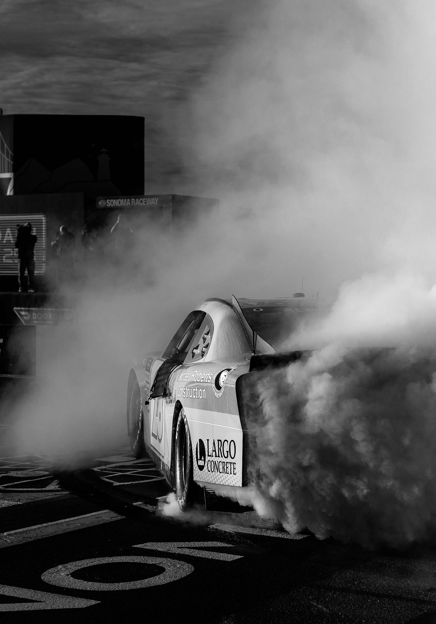 Black and white photo of a race car doing a burnout, surrounded by thick tire smoke at Sonoma Raceway.