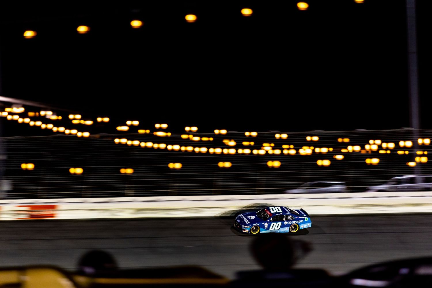 NASCAR race car speeds around a track at night, with bright lights illuminating the circuit in a thrilling evening race.