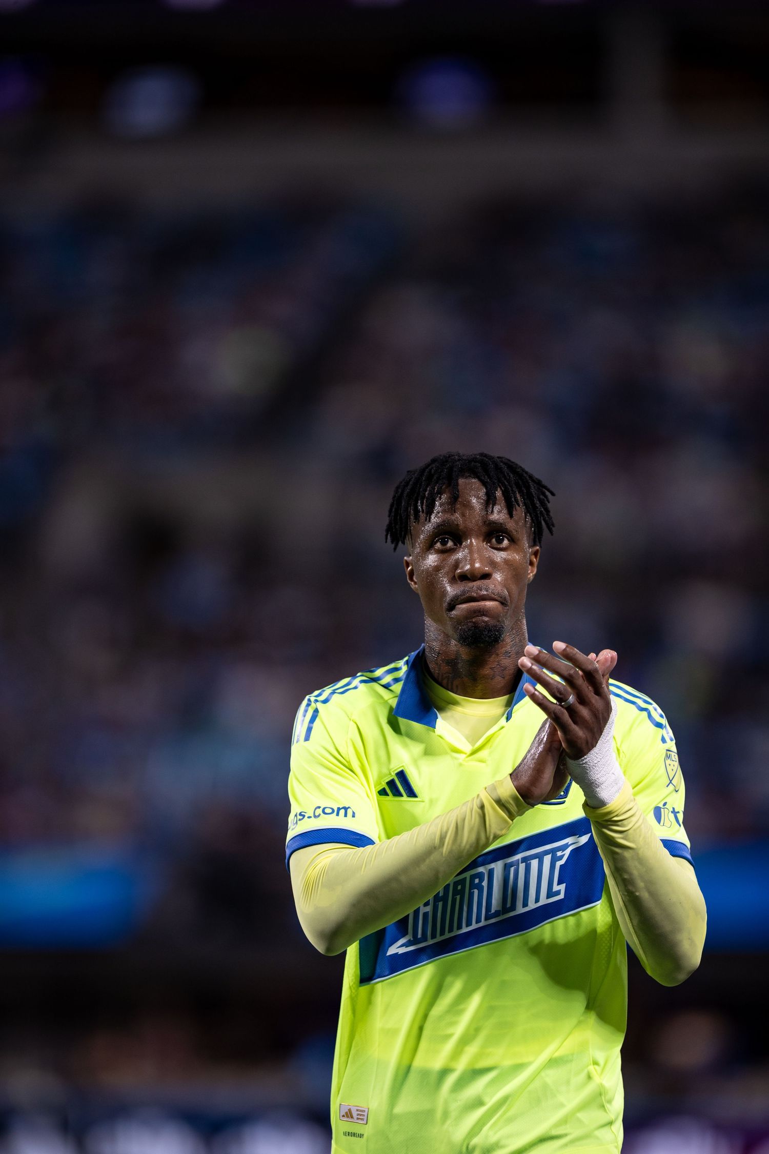 Soccer player in neon yellow Adidas jersey applauds fans on the field during a night match.