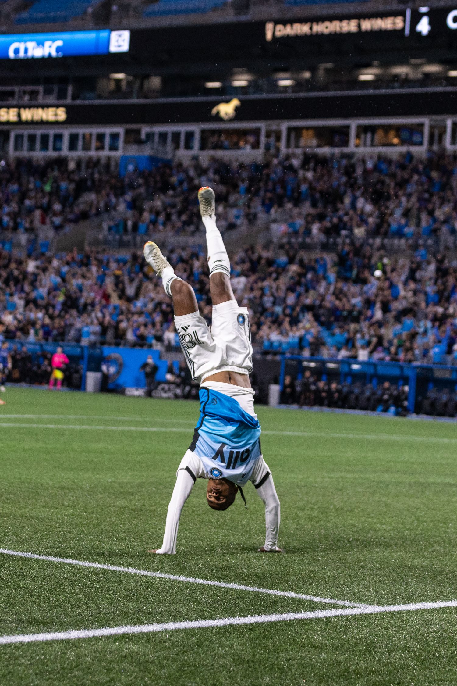 Soccer player performs a handstand celebration on the field during an MLS match at a packed stadium.