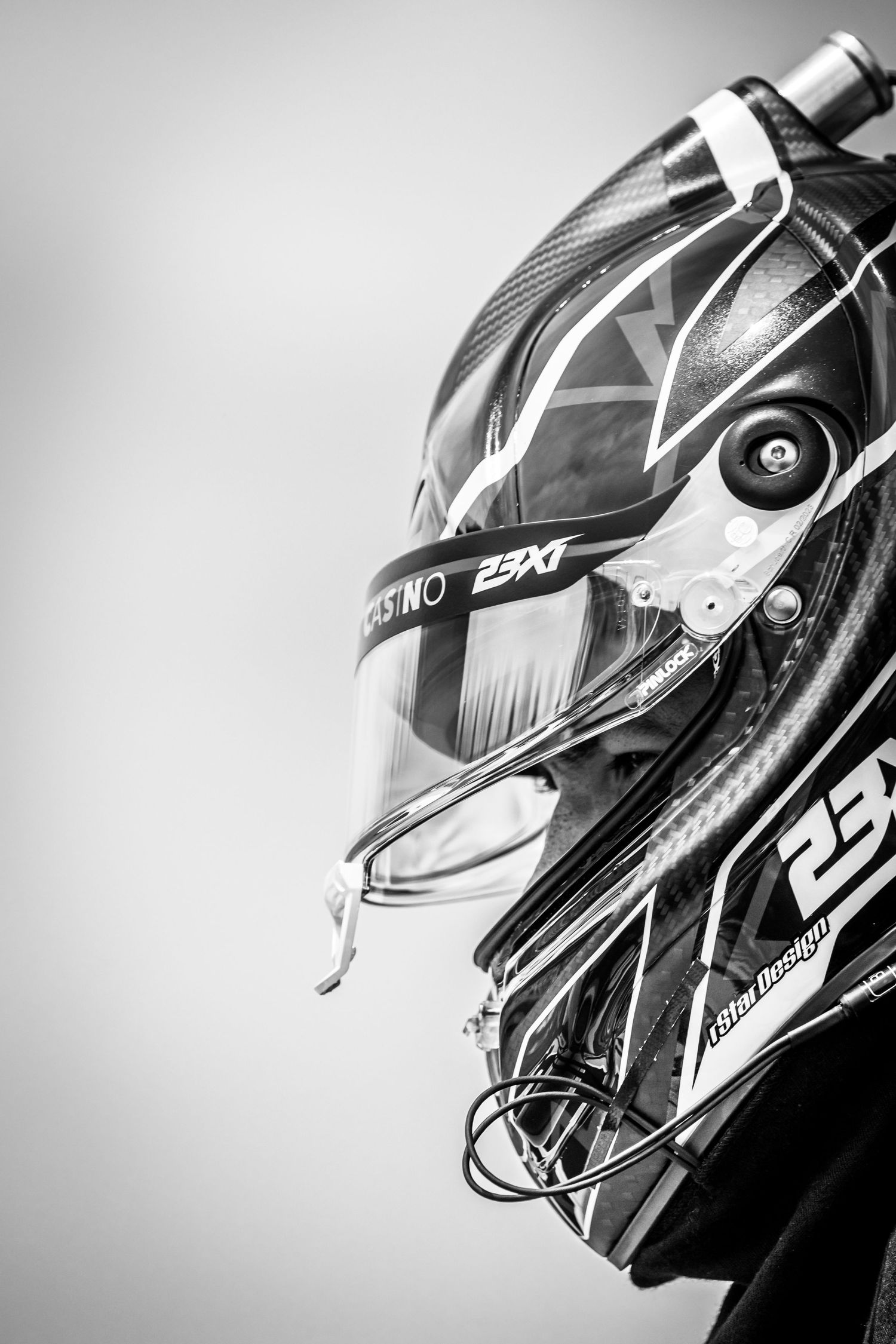 Black and white close-up of a racing driver's helmet featuring 23XI team branding and visor detail.