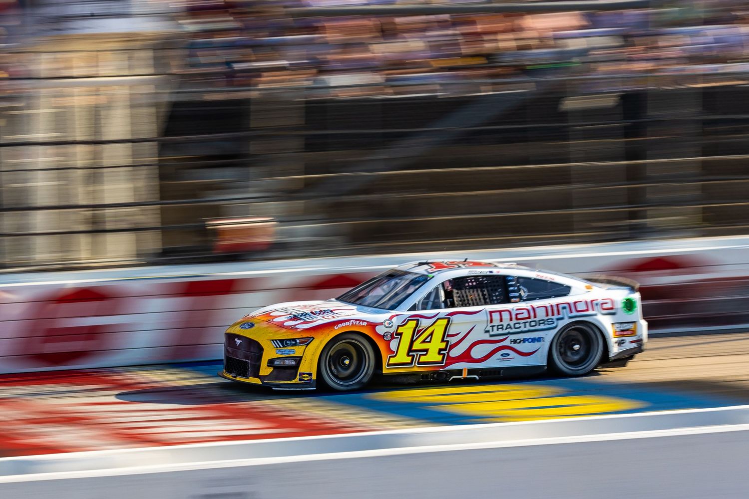 NASCAR #14 race car speeds past pit lane barriers during a sunny day at a road course race track.