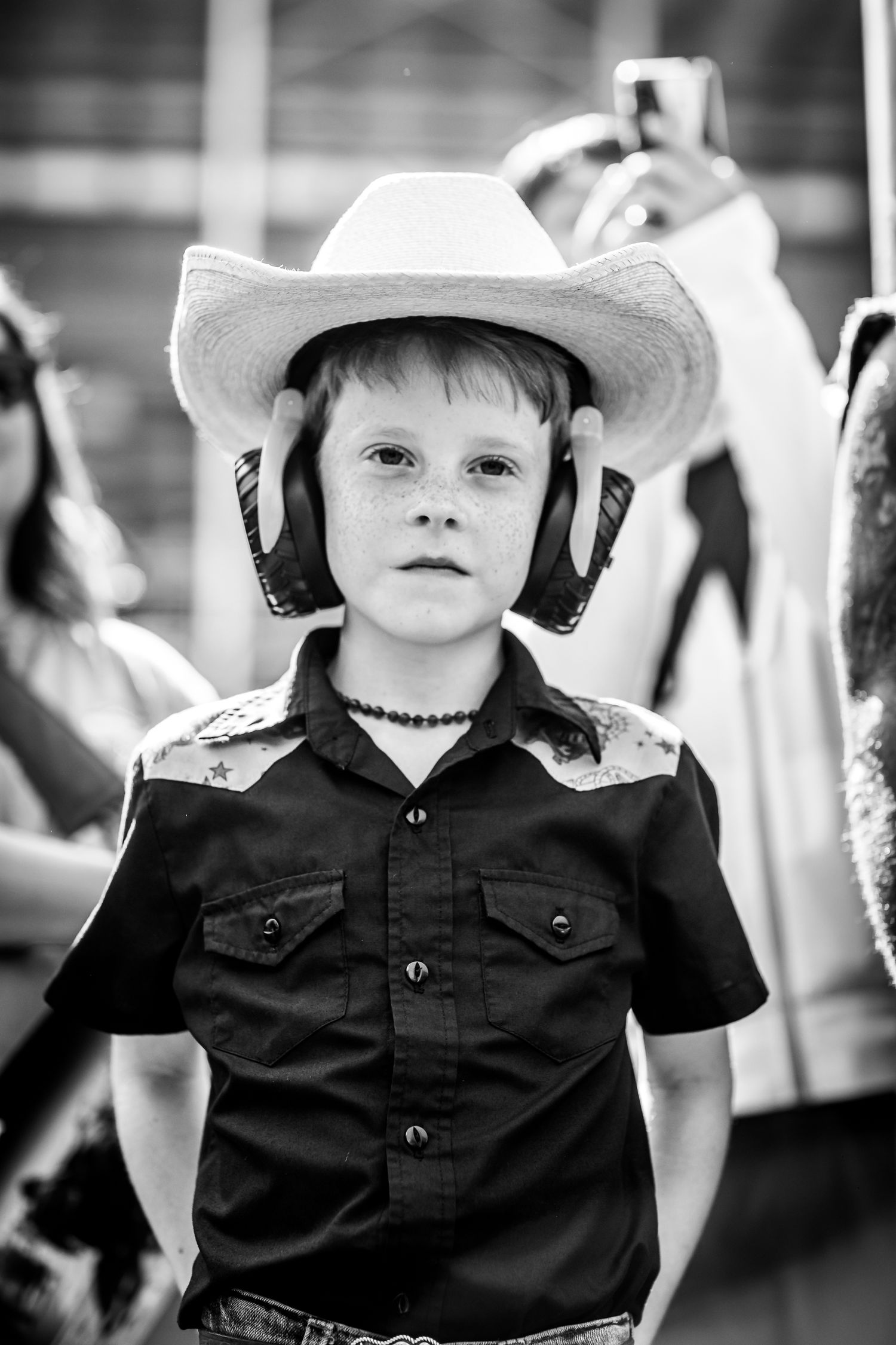 Black and white photo of a young boy wearing a cowboy hat and western shirt at a rodeo event.