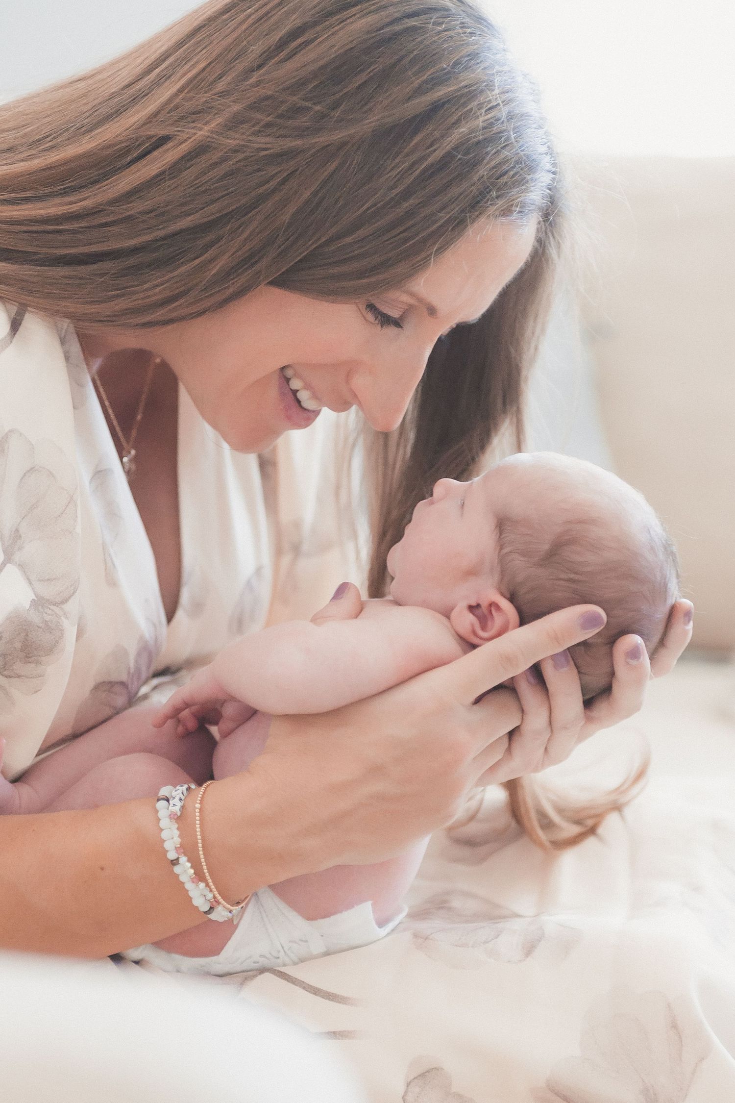 Smiling mother tenderly holds her newborn baby close, sharing a precious bonding moment in soft natural light.