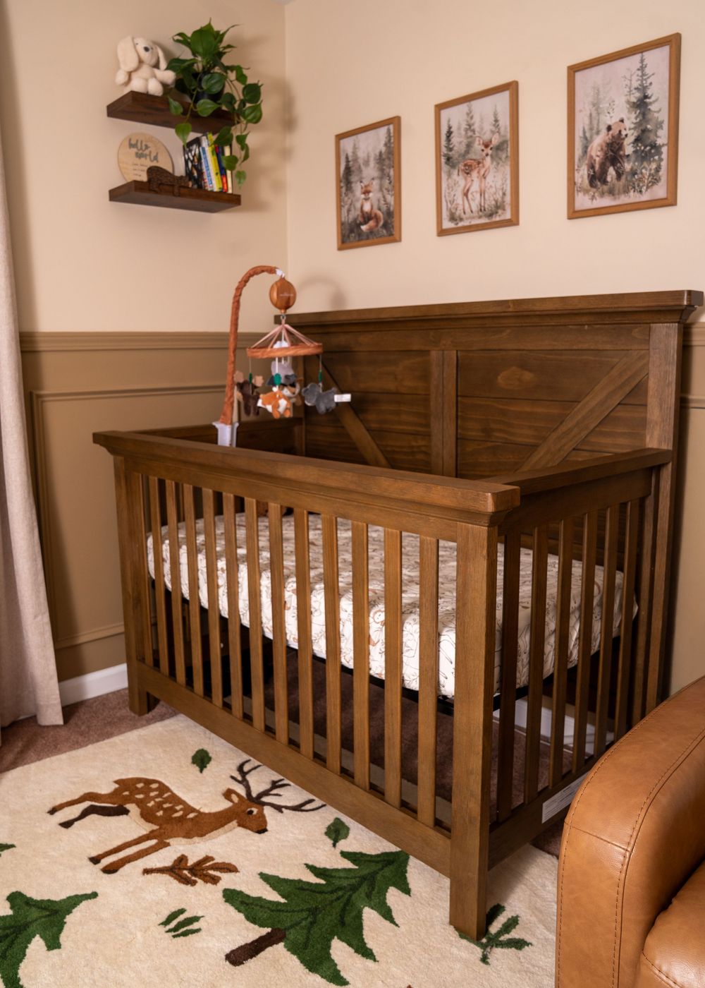 Rustic brown wooden baby crib with nature-themed nursery decor, woodland rug, and framed animal prints on beige walls.
