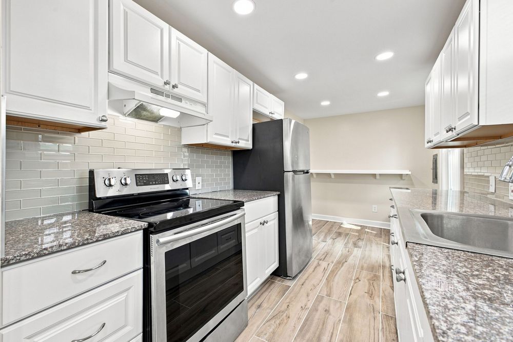 Modern kitchen with white cabinets, granite countertops, stainless steel appliances, and subway tile backsplash on light wood floors.
