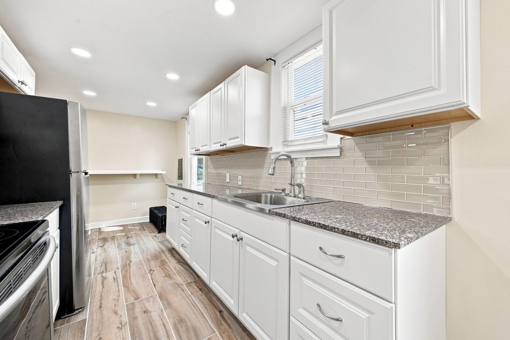 Modern kitchen with white cabinets, granite countertops, stainless steel sink, subway tile backsplash, and light hardwood floors.