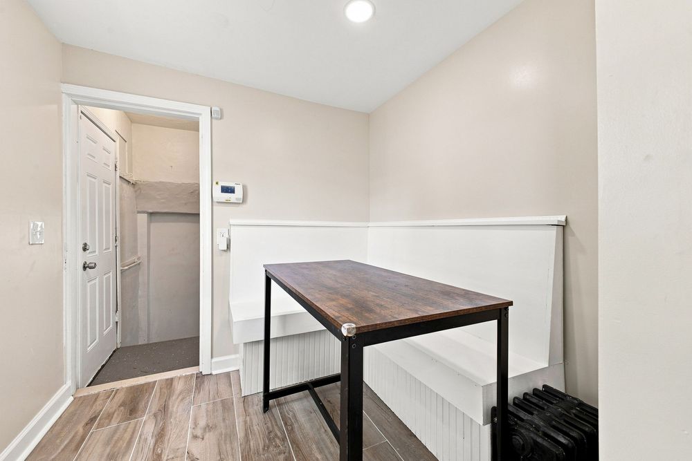 A minimalist mudroom with wood-look flooring, white wainscoting, a dark wood console table, and an open door leading to an entryway.