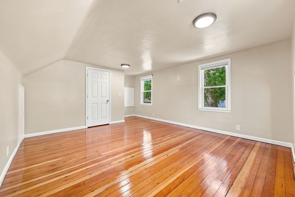 Airy attic bedroom with shiny hardwood floors, sloped ceiling, white door, and a window with garden views.
