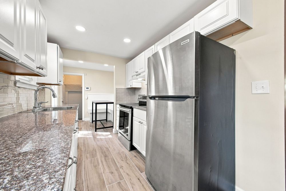 Modern kitchen with stainless steel appliances, white cabinets, granite countertops, and light wood-look flooring.