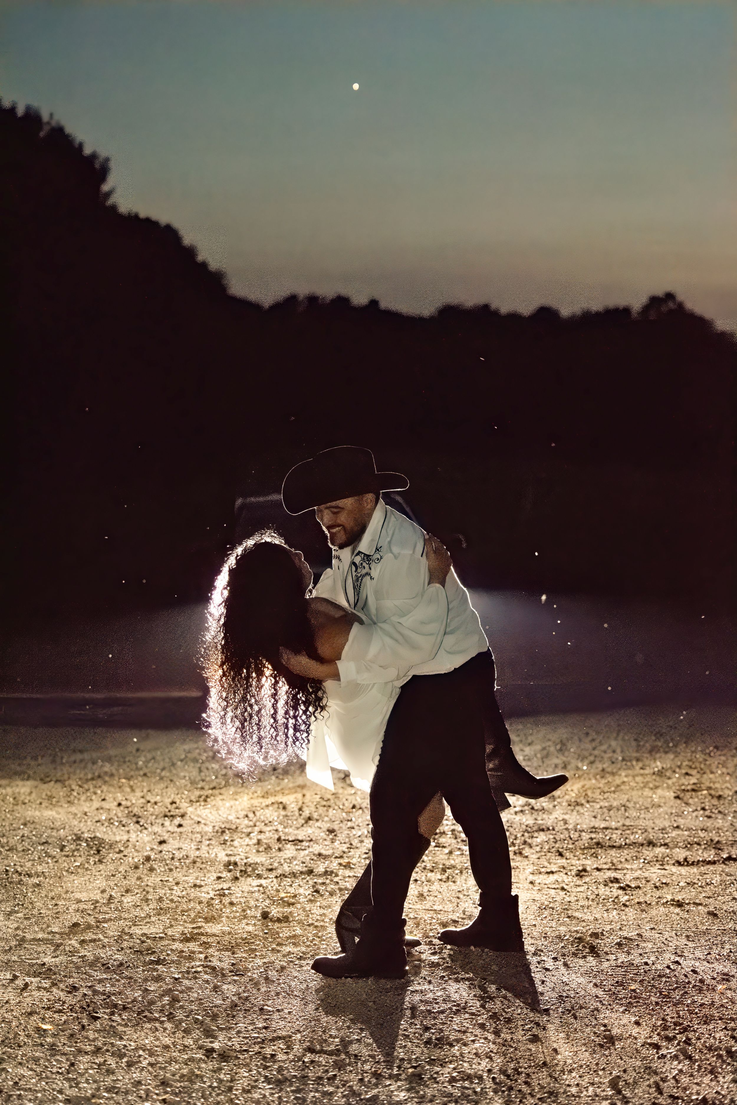 Couple dancing romantically outdoors at night, man in cowboy hat dipping woman under starry sky with glowing light effects.