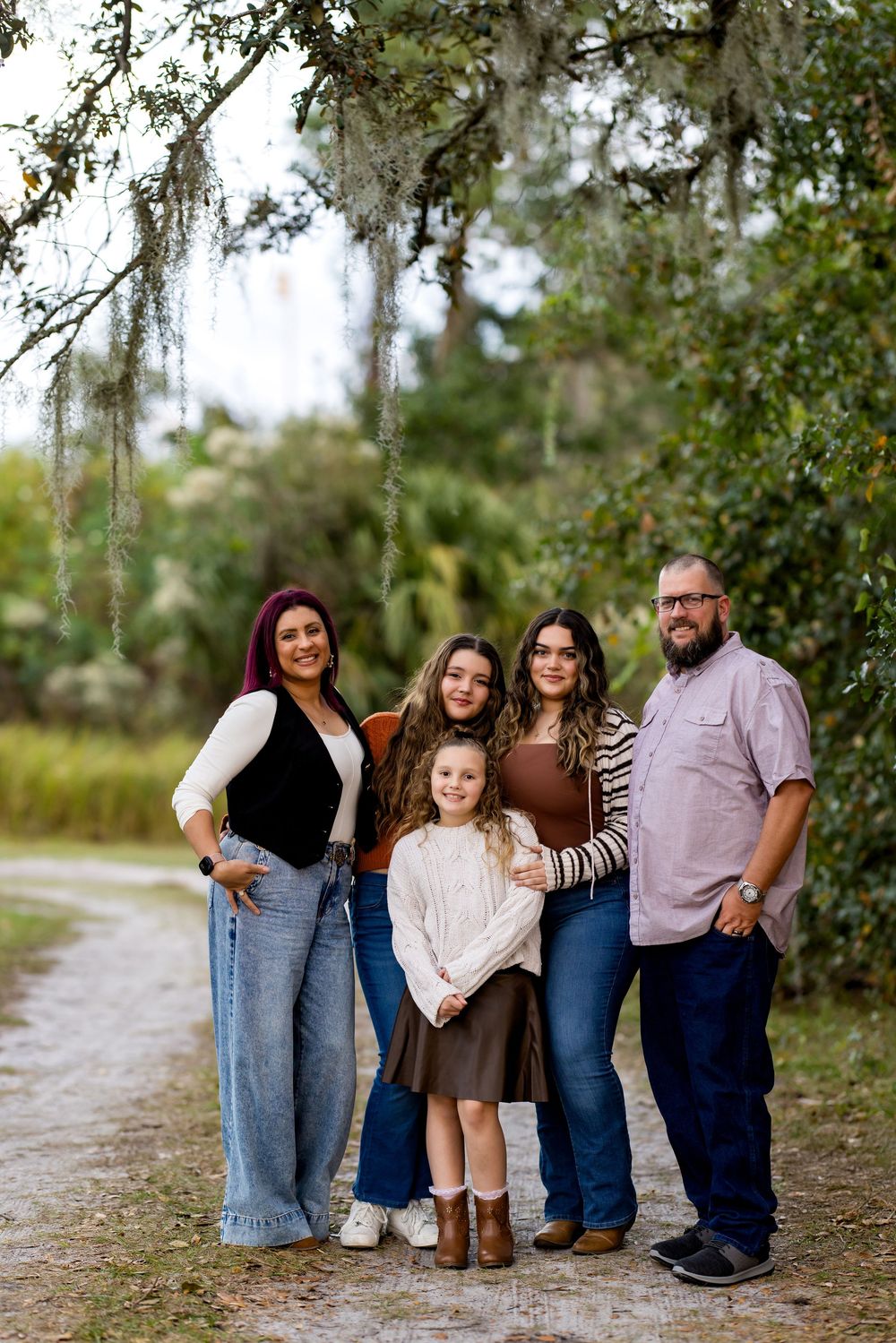 Family of five posing on a scenic tree-lined path with Spanish moss, dressed in coordinated fall outfits.