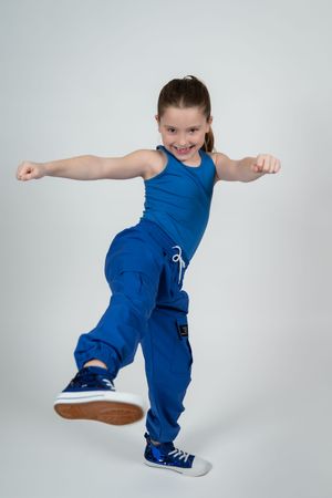Young girl in blue outfit striking a dynamic dance pose with arms extended and one leg raised.