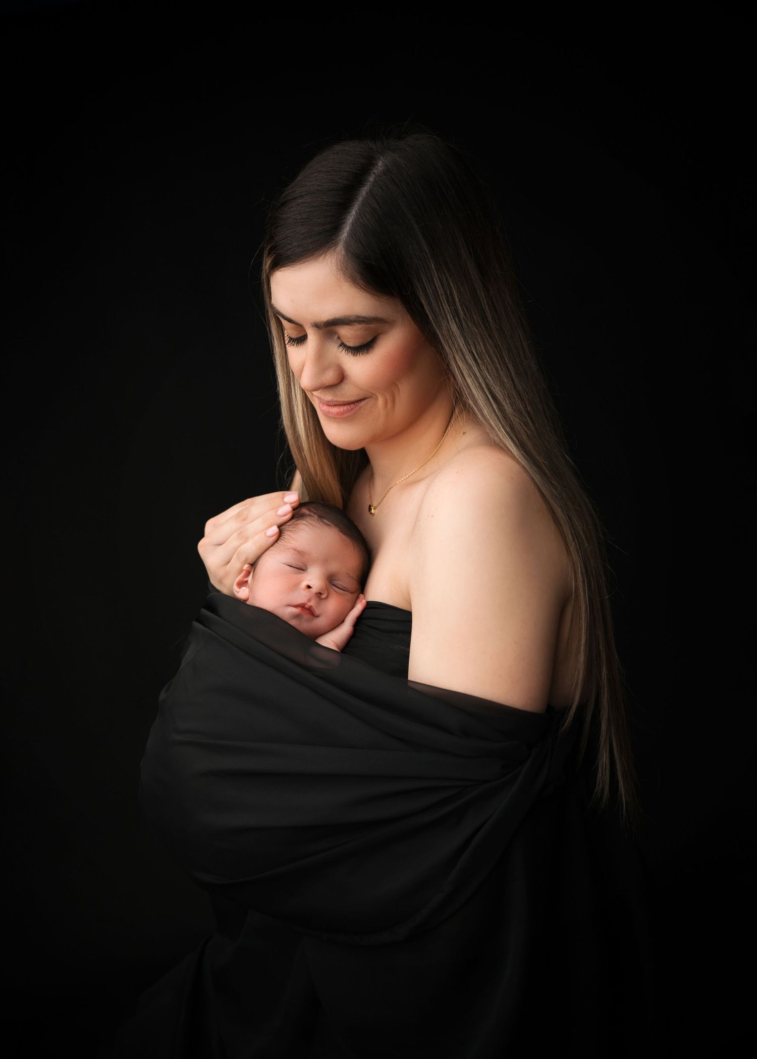 Mom wrapped with her newborn in a black fabric in studio in linden NJ