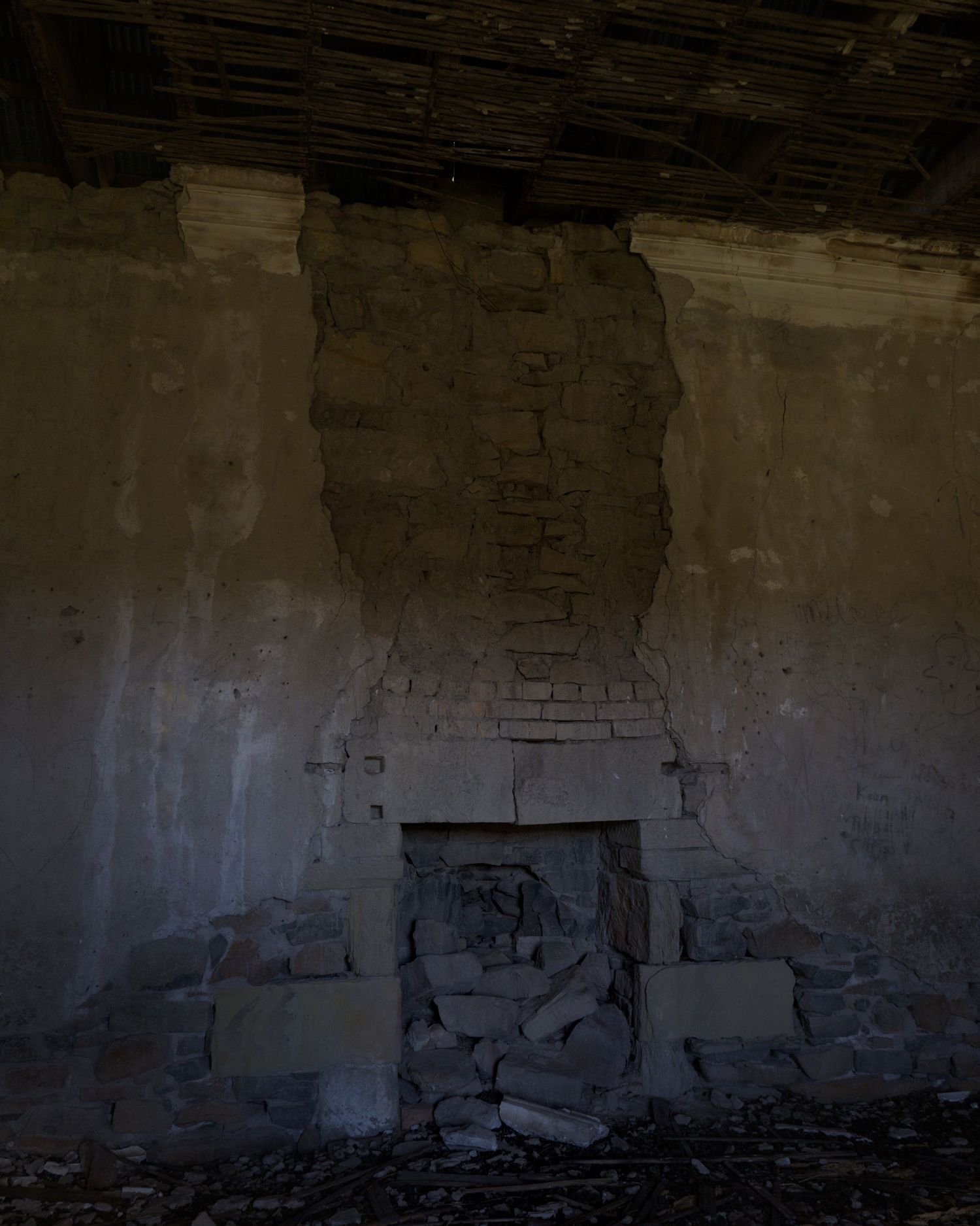 Abandoned room with crumbling brick fireplace, rubble pile, and deteriorating plaster walls in a derelict building.
