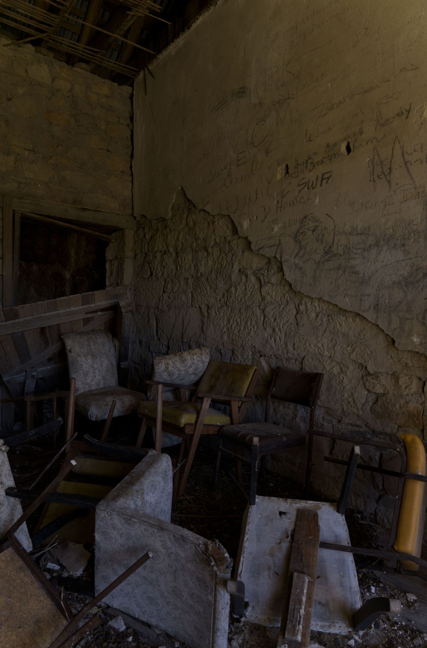 Abandoned room with deteriorating walls, graffiti, and scattered broken chairs amid debris and rubble.