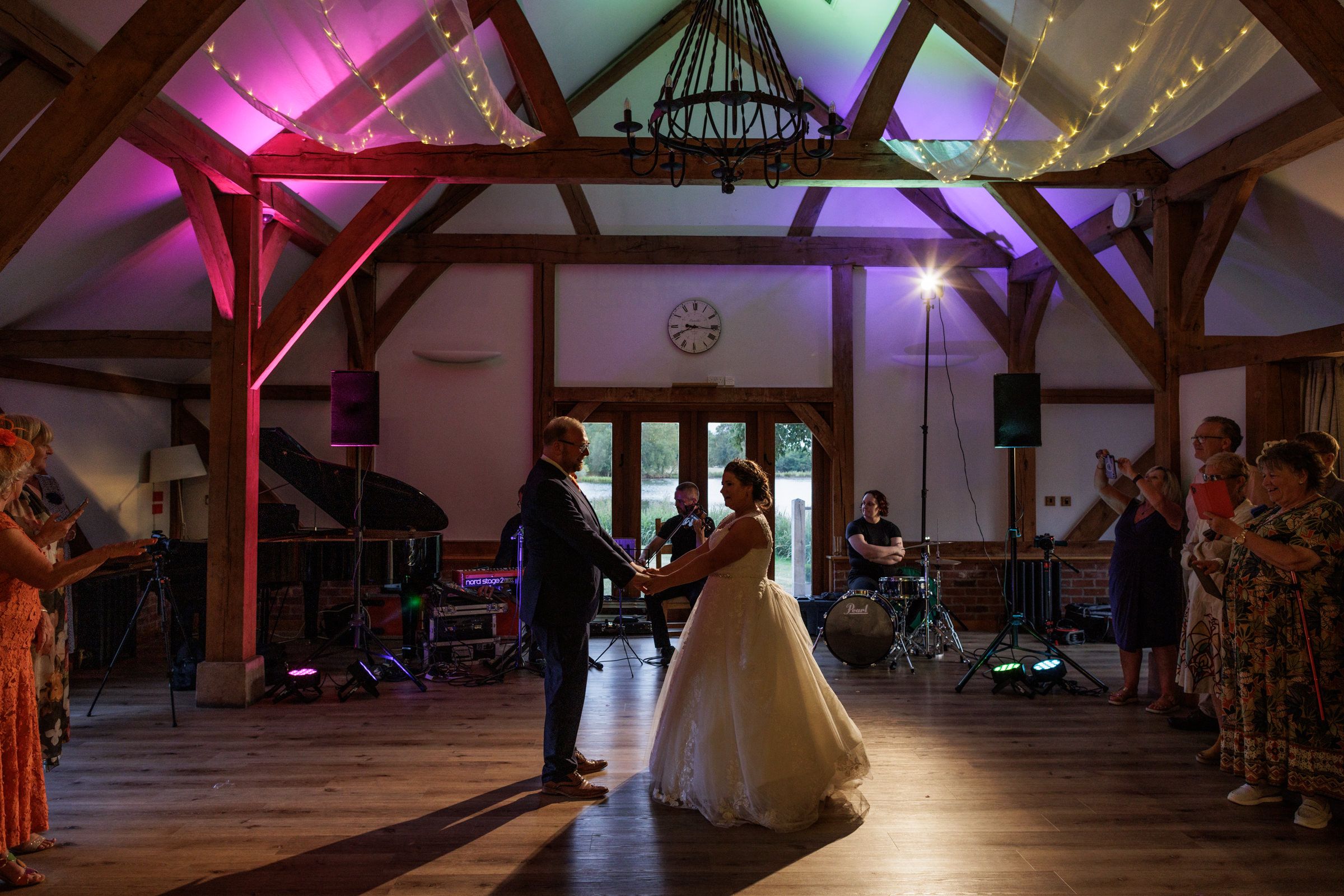 Bride and groom share first dance in elegant barn venue with fairy lights and purple uplighting during wedding reception.