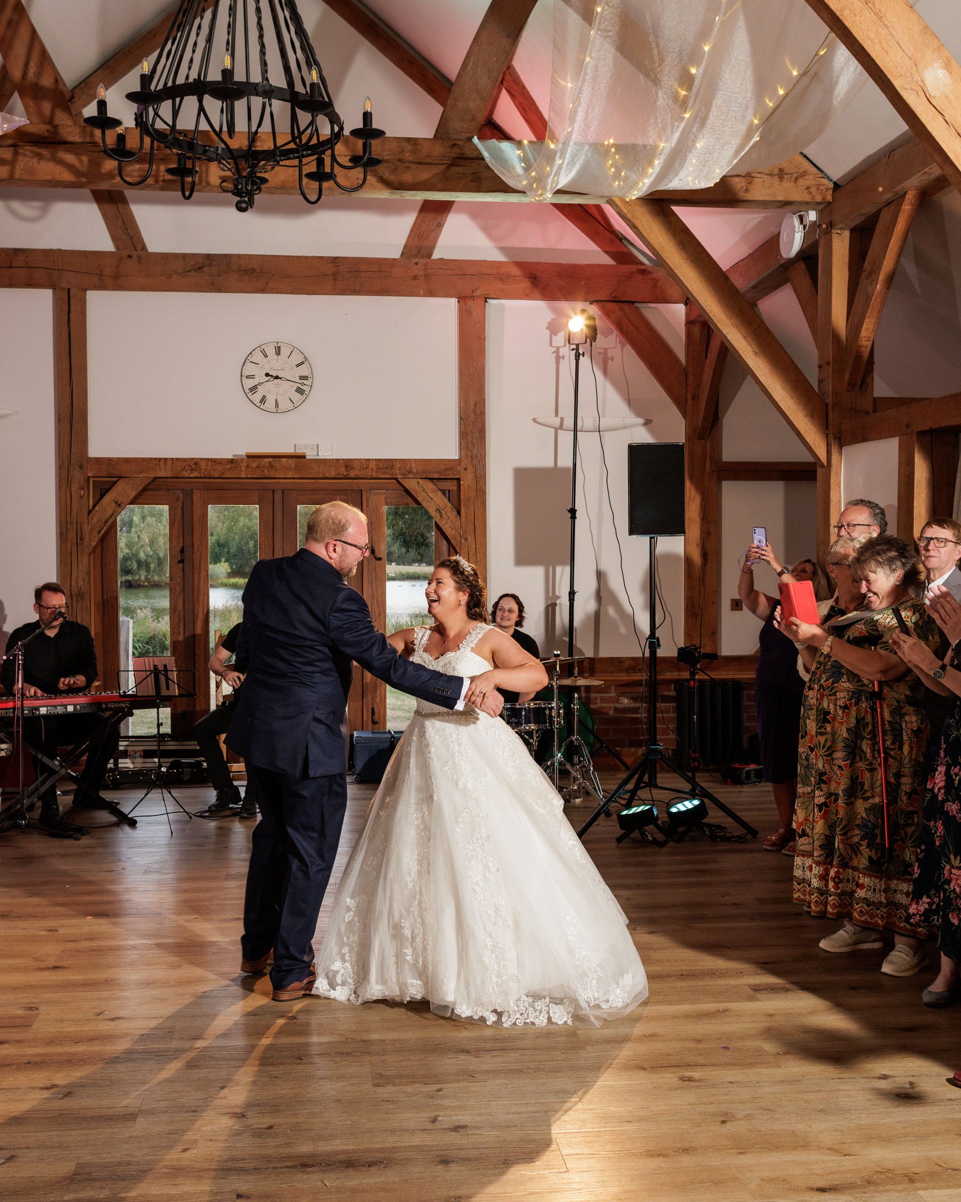 Bride and groom share their first dance in a rustic barn wedding venue with wooden beams and fairy lights.
