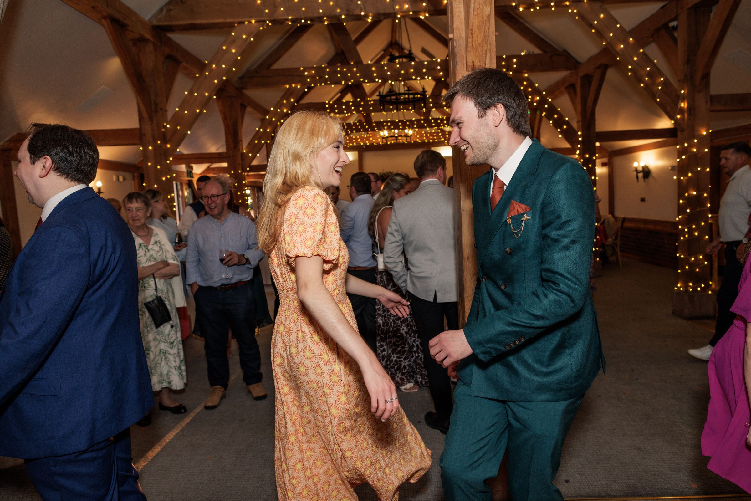 Couple dancing and laughing together at an elegant wedding reception venue with warm fairy lights and wooden beams.