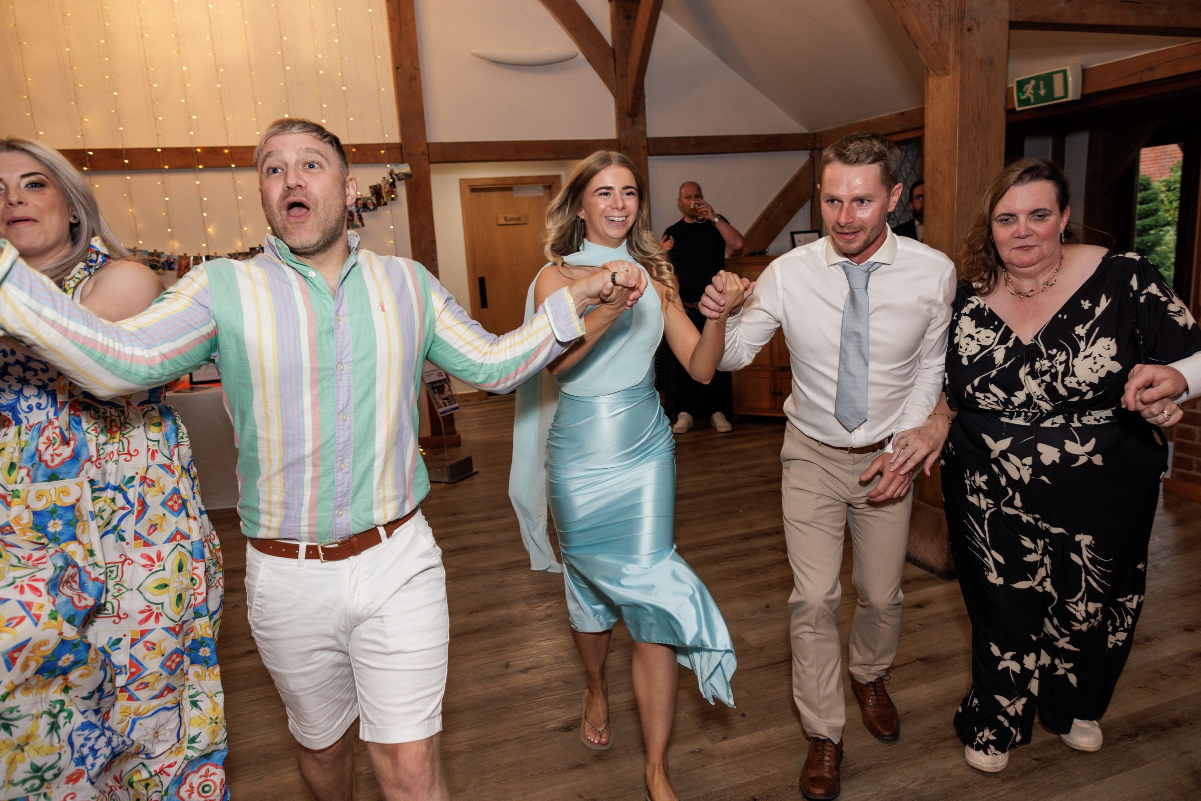 Group of guests dancing joyfully at a wedding reception in a rustic barn venue.