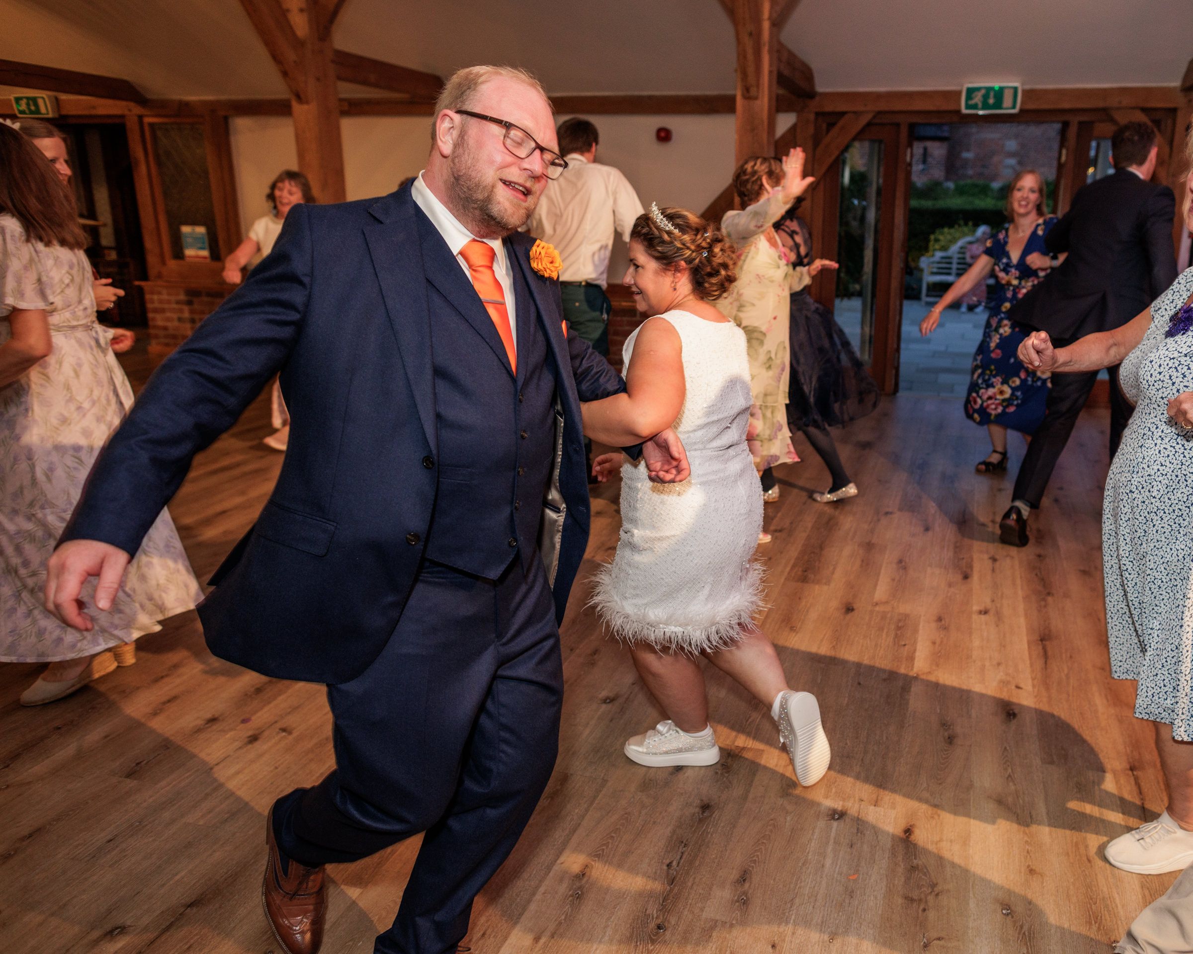 Bride and groom dancing joyfully at wedding reception in rustic barn venue with guests celebrating in background.