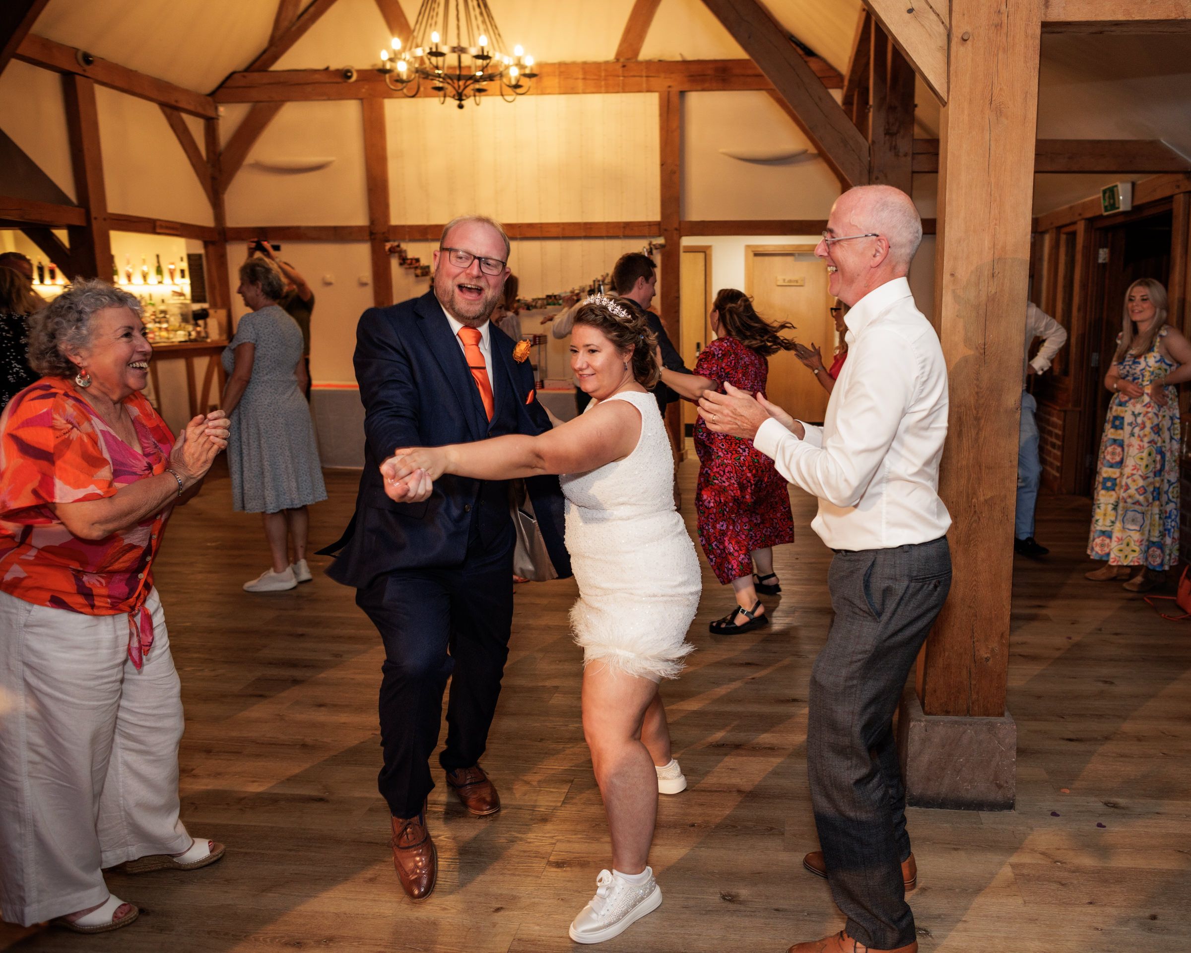 Guests dancing joyfully at a rustic wedding reception in a barn venue with warm lighting.
