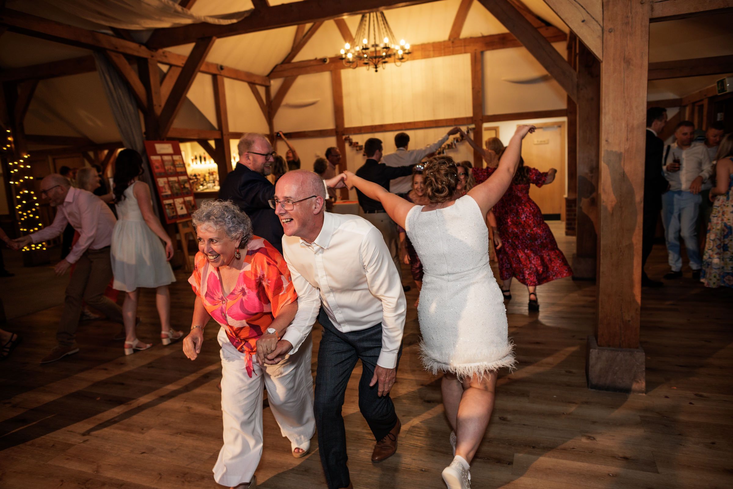 Guests dancing joyfully at a rustic barn wedding reception with wooden beams and warm lighting.