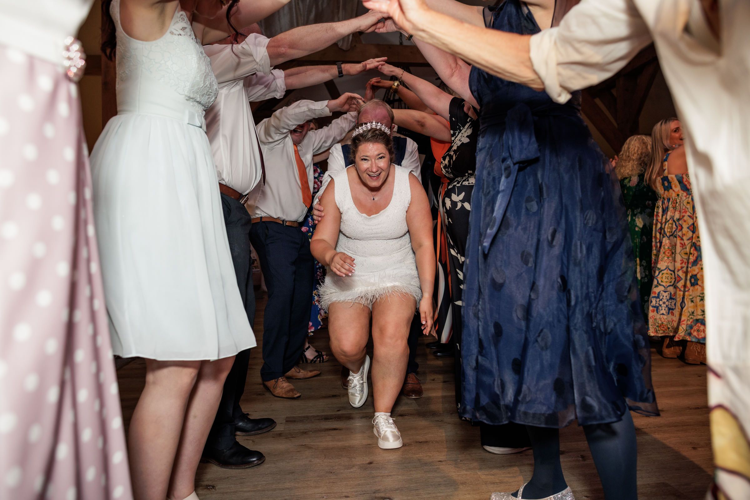 Bride in white dress excitedly running through a tunnel of guests at wedding reception.