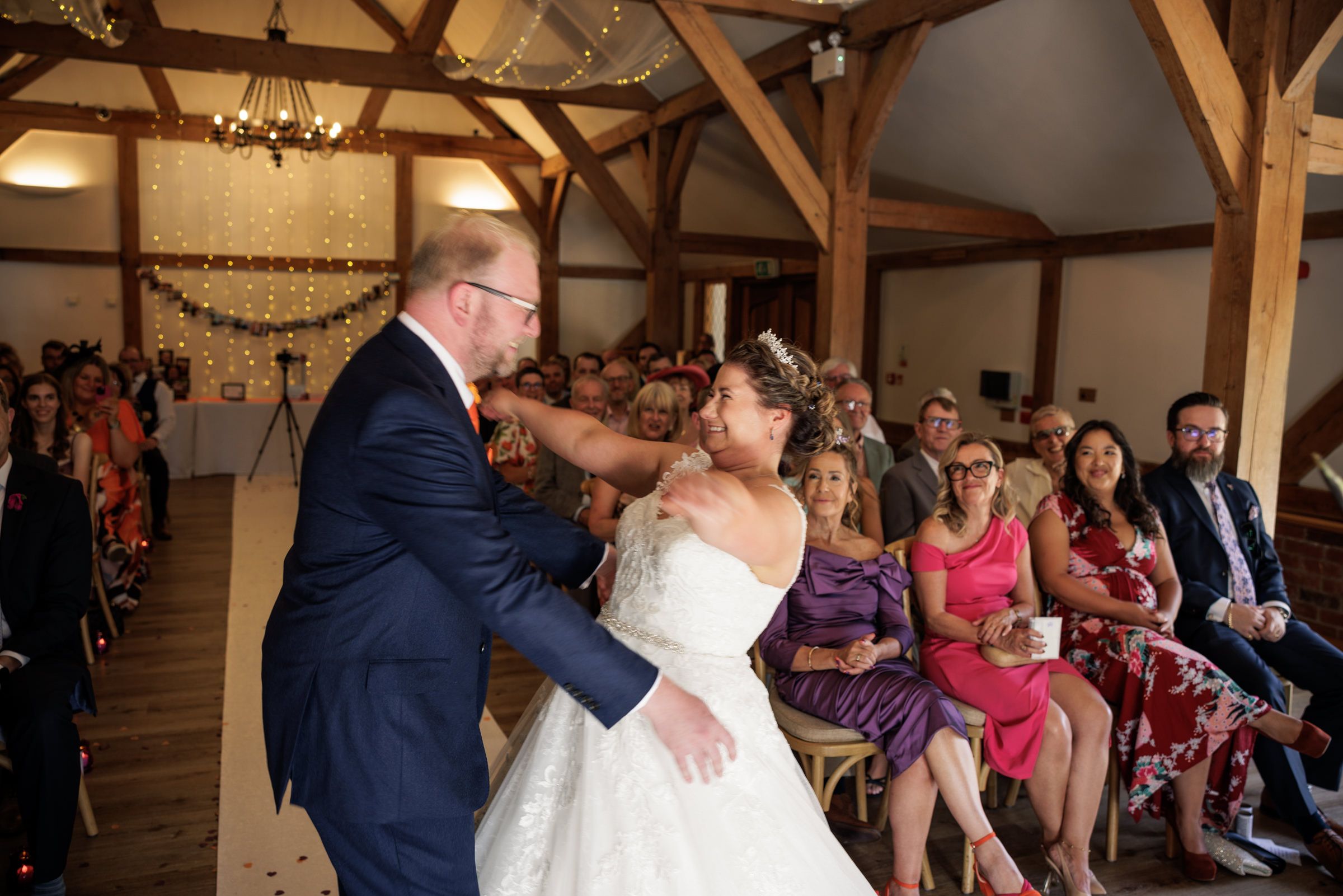 Bride and groom share a tender moment during their wedding ceremony in a rustic barn venue with guests seated nearby.