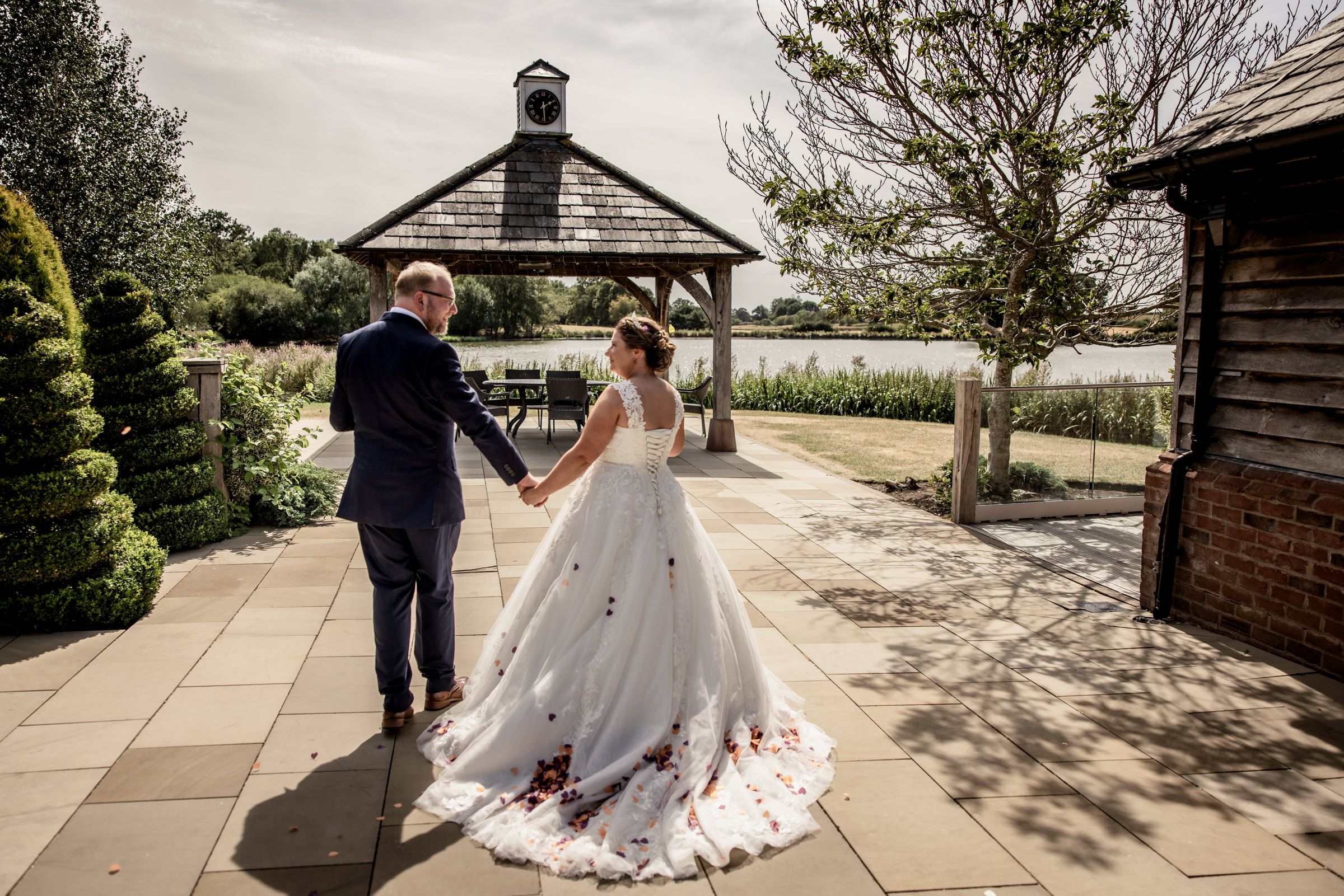 A bride and groom hold hands walking toward a gazebo in a scenic garden on their wedding day.