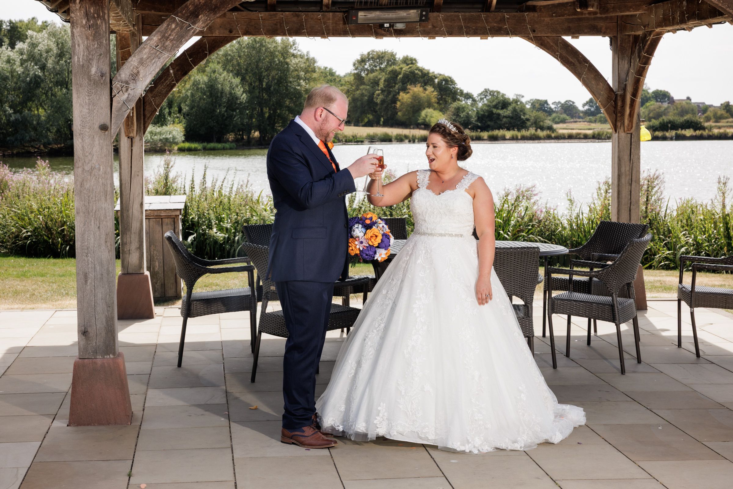 Bride and groom sharing a romantic moment under a wooden pergola by a lake on their wedding day.