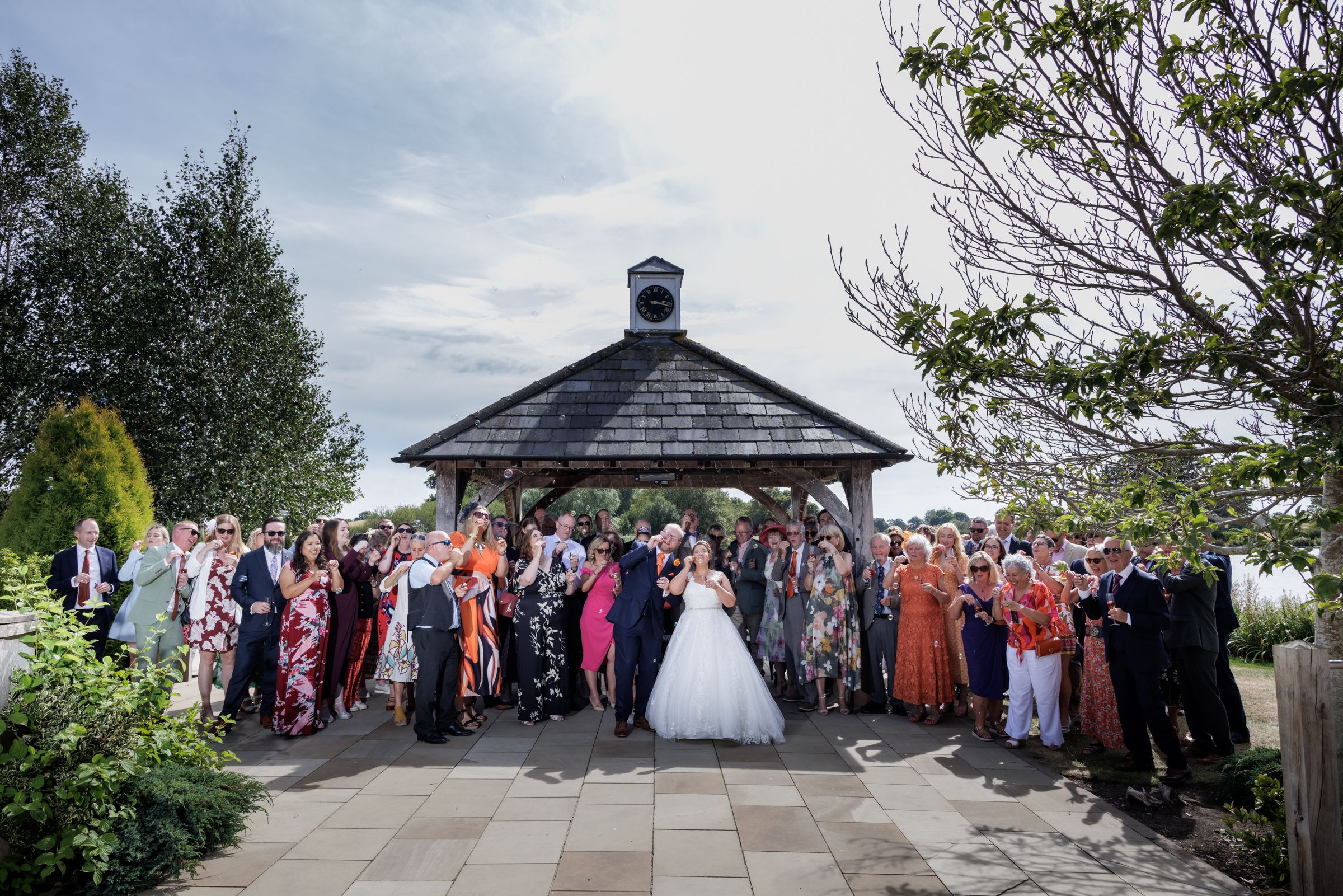 Wedding couple kiss surrounded by guests near a gazebo in an outdoor garden ceremony venue.