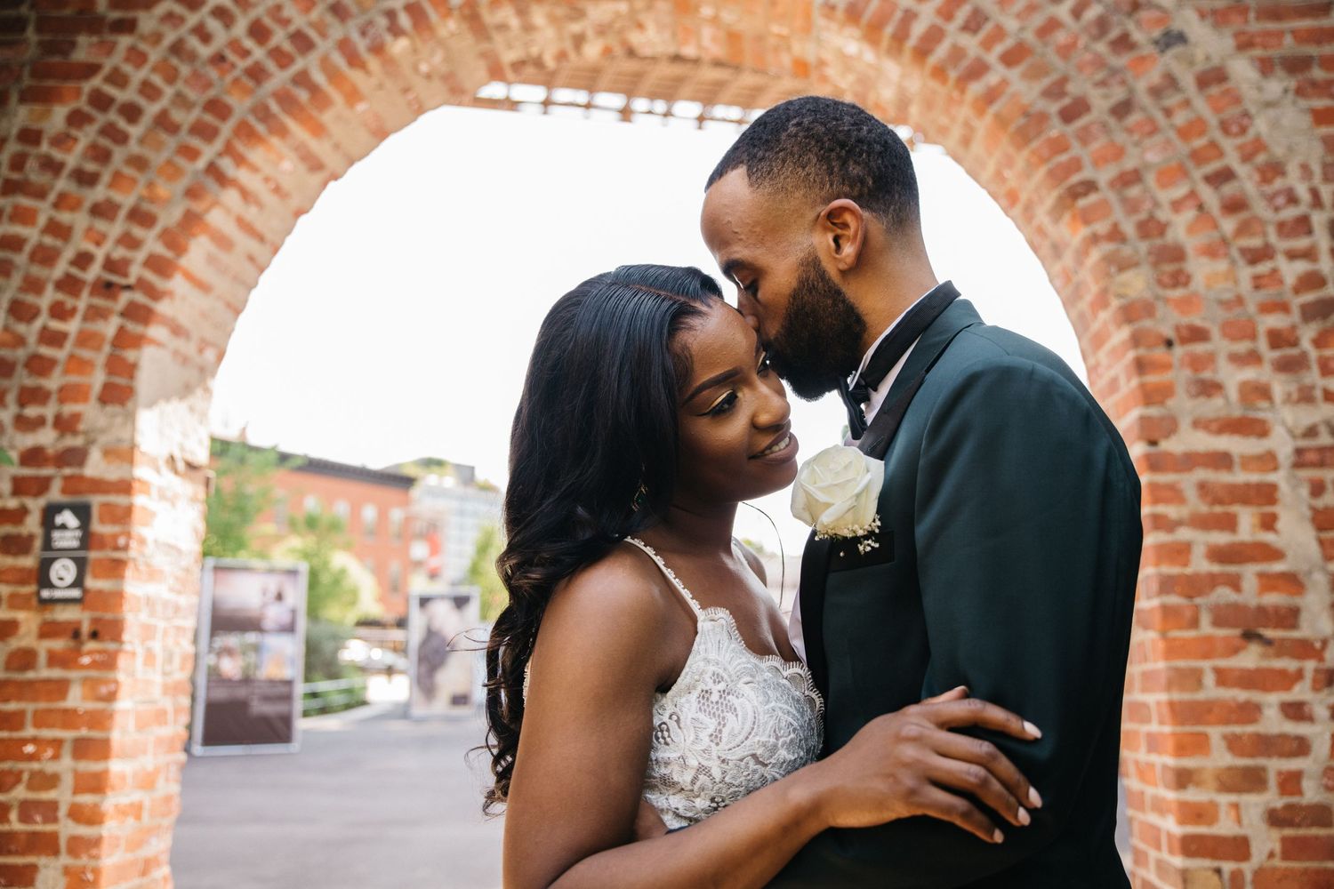 A romantic moment captured under a brick archway during a wedding.