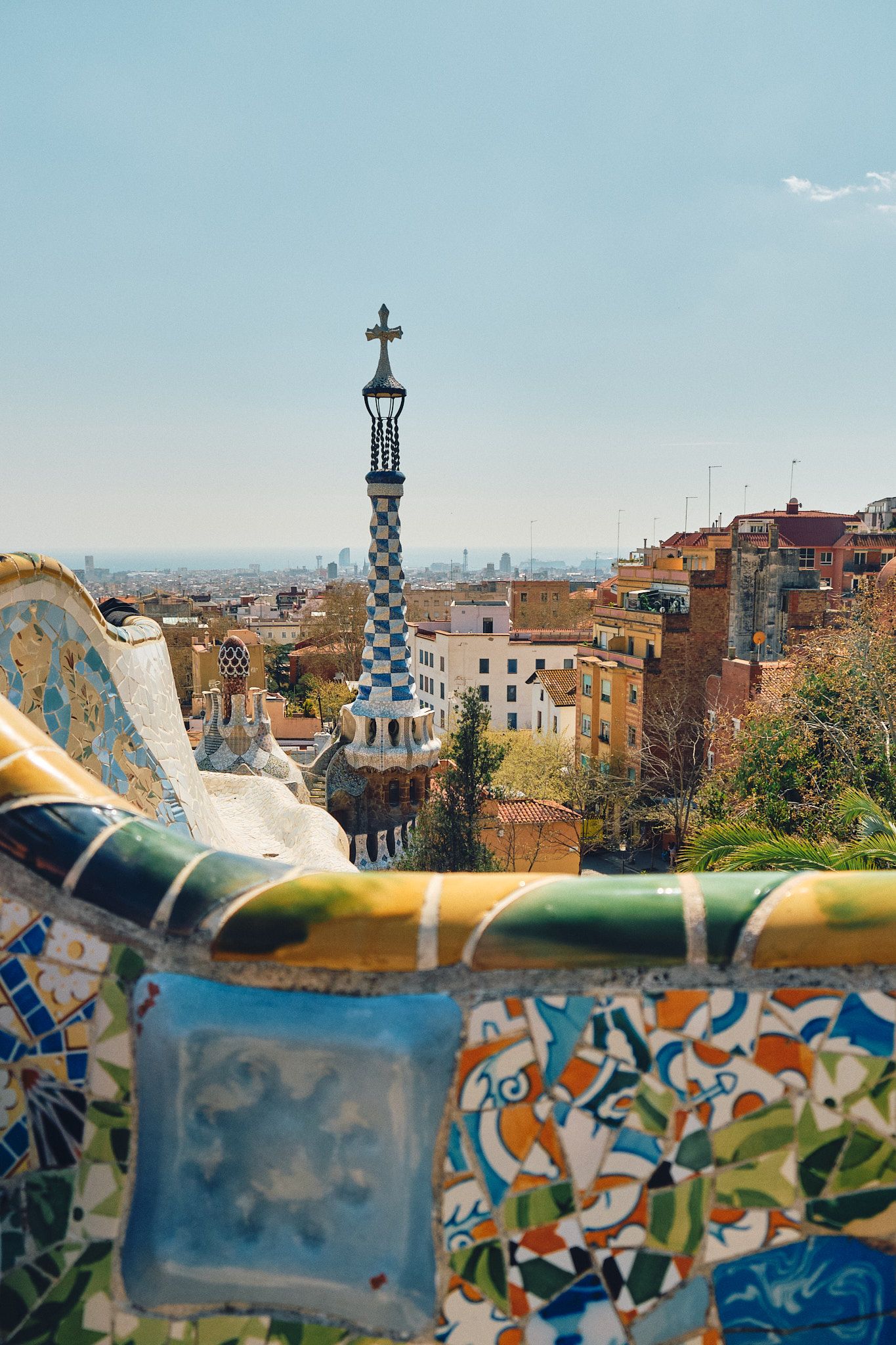 Colorful mosaic benches at Park Güell, Barcelona, with a checkered tower and city skyline in the background.