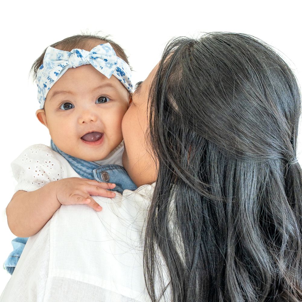 Smiling six-month-old baby in a blue bow being held against her mother’s shoulder.