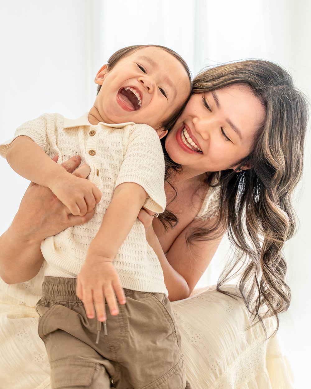 Mother laughing while holding her smiling toddler during a studio portrait session.