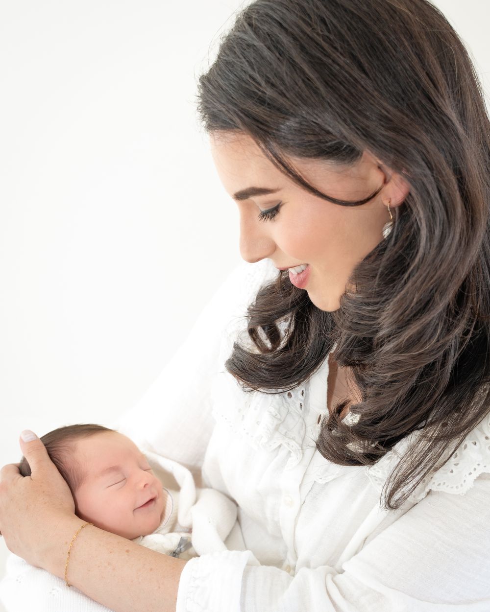 Mother looking down at her newborn baby while holding them against a bright white background.