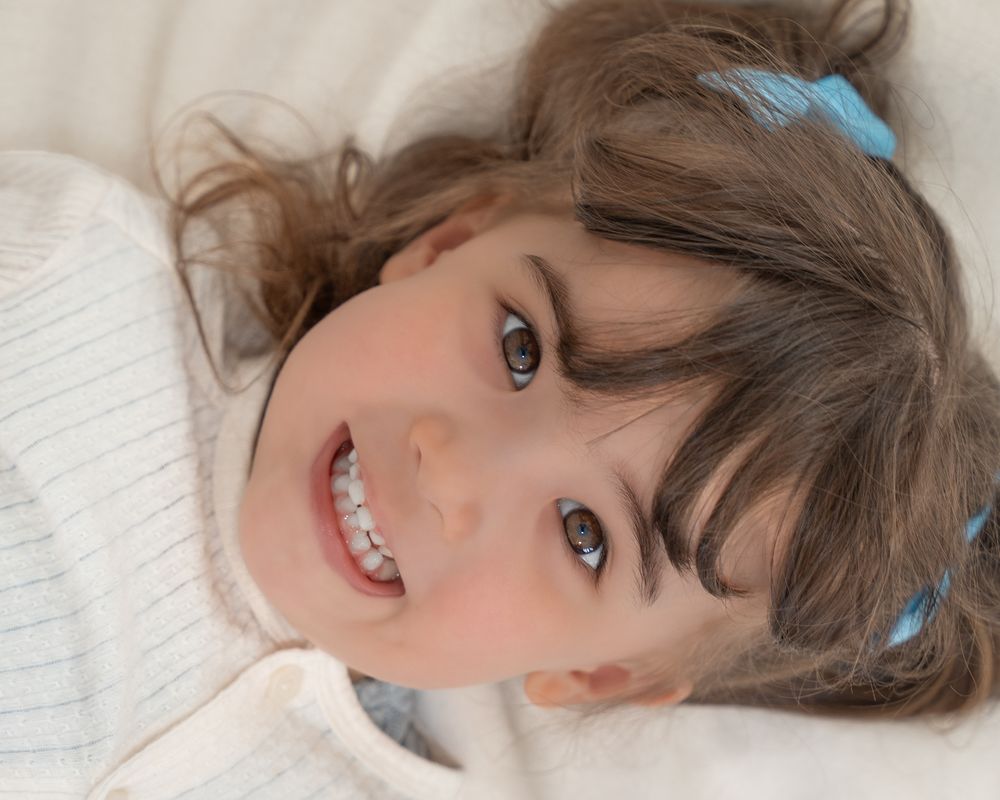 Young girl smiling while lying on soft white blankets during a studio portrait session.