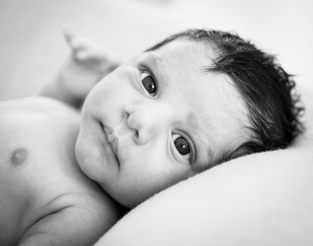 Awake newborn lying on a soft blanket in a black-and-white close-up portrait.
